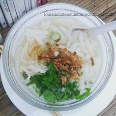 a bowl filled with noodles, meat and parsley on top of a wooden table