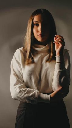 a woman in a white sweater and black skirt posing for the camera with her hands on her hips