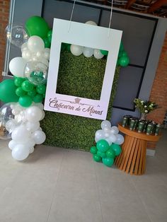 an arrangement of green and white balloons in front of a photo frame on the wall