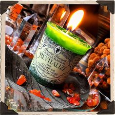 a green candle sitting on top of a table next to some rocks and glass bottles