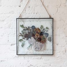 a painting hanging on a white brick wall with flowers and leaves in the frame above it