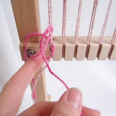 a person is weaving pink yarn on a wooden loom with two pins in it