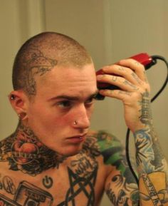 a man with tattoos holding a hair dryer up to his head and looking at the camera