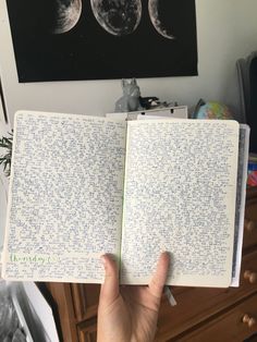 a hand holding an open notebook with writing on it in front of the moon phases