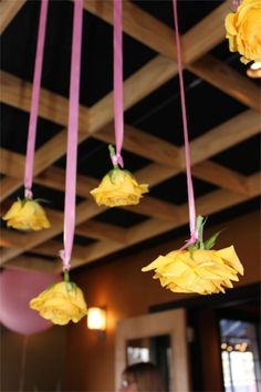 yellow flowers are hanging from the ceiling with pink ribbon around them and some people in the background