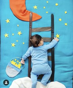 a baby laying on top of a blue blanket next to a wooden ladder with yellow stars