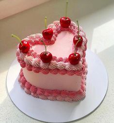 a pink heart shaped cake with cherries on the top is sitting on a white plate