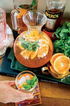 a person is holding a glass pitcher filled with oranges and minty tea on a tray