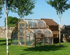 a house made out of wood and glass in the middle of some grass with trees next to it