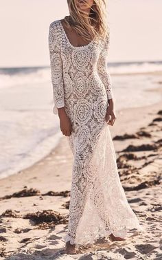 a woman standing on top of a sandy beach next to the ocean wearing a white dress