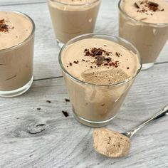 three glasses filled with different kinds of desserts on top of a wooden table next to a spoon