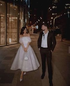 a man and woman in formal wear standing next to each other on a sidewalk at night