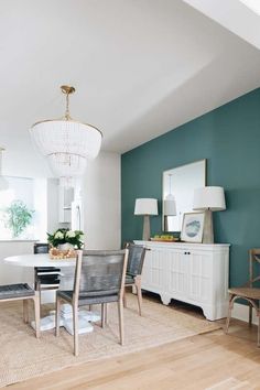 a dining room with blue walls and white furniture in the center, along with a chandelier hanging from the ceiling