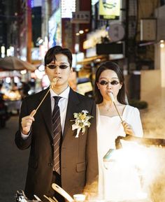 a man and woman standing next to each other in front of a street with lights