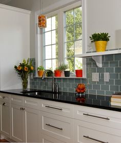 a kitchen with white cabinets and black counter tops next to a window filled with potted plants