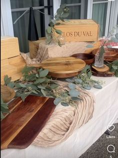 a table topped with lots of wooden cutting boards covered in leaves and greenery next to a sign that says los duval