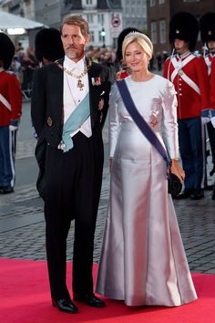 a man and woman standing next to each other on a red carpet in front of soldiers