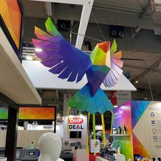 a colorful bird sculpture hanging from the ceiling in a building with other items on display