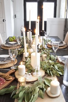 a dining room table with candles and greenery on the placemats for dinner