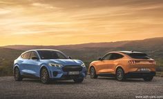 two electric vehicles parked next to each other in front of a mountain range at sunset