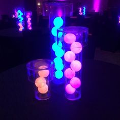 several lit up vases sitting on top of a table in front of purple and blue lights