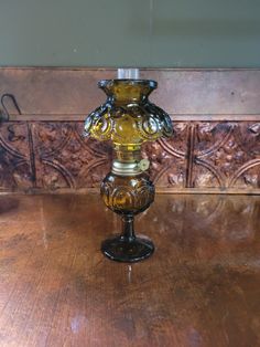 a glass candle holder sitting on top of a wooden table in front of a wall