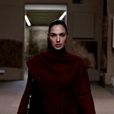 a woman walking down a hallway in a red coat and black pants with her hand on her hip