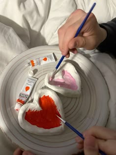 someone is painting hearts on a plate with paintbrushes and some other things in front of them