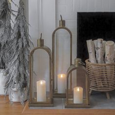 three lit candles sitting on top of a wooden table next to a basket filled with logs