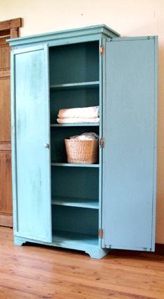 an old blue cabinet with baskets and towels in the bottom shelf is shown on a hard wood floor