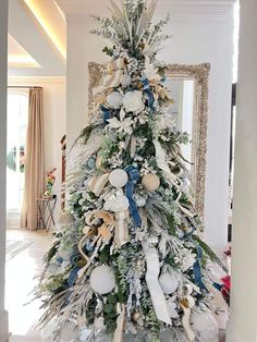 a white christmas tree with blue and gold decorations in a living room next to a mirror