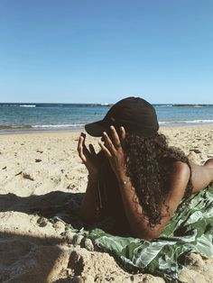 a woman laying on top of a sandy beach next to the ocean holding her hands up