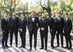 a group of men in suits standing next to each other on a wooden bridge with trees behind them