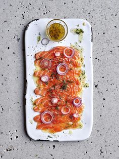 a white plate topped with salmon and onions next to a small bowl of dipping sauce