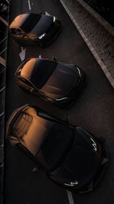 two black sports cars parked next to each other on the side of a road at night