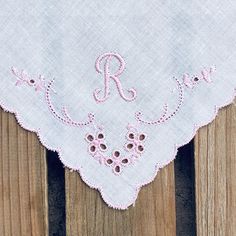 a close up of a wooden surface with a table cloth on it that has embroidered letters and flowers