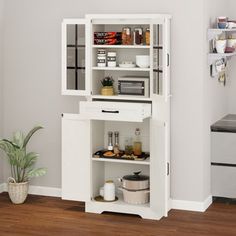 a white cabinet with some food on it in a room next to a potted plant