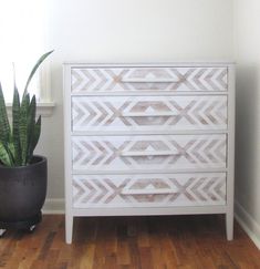 a white dresser sitting next to a potted plant on top of a hard wood floor