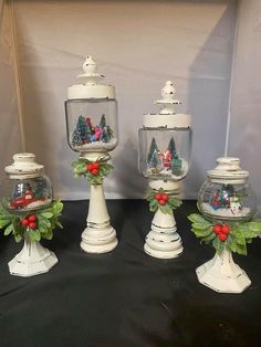 four glass vases with christmas decorations on them sitting on a black cloth covered table