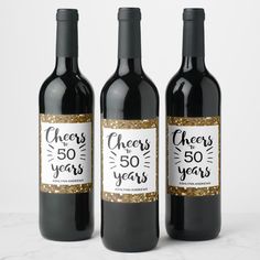 three bottles of wine with gold glitter on the bottom and cheers to 50 years label