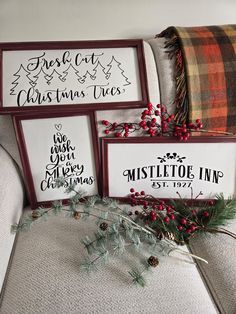 three framed christmas signs sitting on top of a couch next to a plaid throw pillow