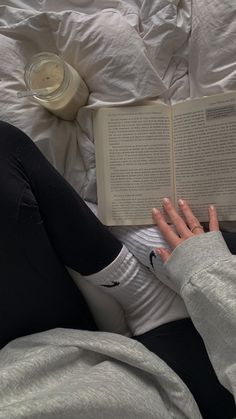 a woman laying in bed reading a book with her hand on the open book's cover