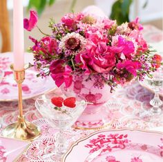 pink flowers in a vase on a table with plates and candlelight holders for centerpieces