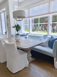 a dining room table with white chairs and blue couches in front of large windows