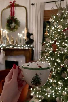 a woman is holding a bowl in front of a christmas tree