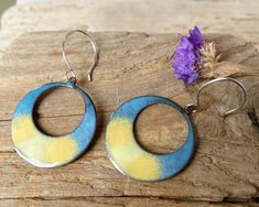 Sunrise Hoop Earrings, torch enameled copper.  Large Yellow blue round enamel earrings. Feel the colors of the sun, bright, warm and inviting. Soak in the rays of the sun, uplifting! Stainless steel or Sterling large hook earwires. (Comes with silicone stoppers to secure the earwire.) The copper enameled shape is 1 1/4″ round, total length approximately 2″. Please note this is a handcrafted item and there are slight variations on the finish. If you would like to see a picture of the one one currently in stock please just message. Handmade in USA. Enameling is glass fused to copper at high heat. Enamels are finely ground glass, like fine sand, also referred to as vitreous enamel. Enameled copper has a durable, glossy finish that doesn't fade under ultraviolet light. Enamels may be opaque or Nickel-free Enamel Round Hoop Earrings, Rays Of The Sun, Enameled Copper, Enamel Earrings, Color Effect, Organza Gift Bags, Enamel Jewelry, Copper Earrings, Handmade Artisan