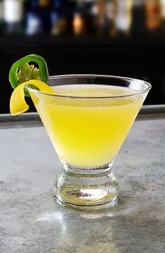 a glass filled with yellow liquid sitting on top of a counter next to a green pepper