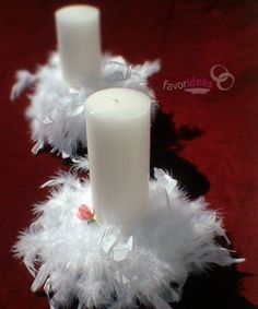 two white candles sitting on top of a red cloth covered table next to each other