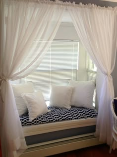 a window seat with white curtains and pillows