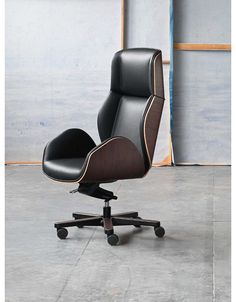 an office chair with black leather upholstered on the back and arms, sitting in front of a wall